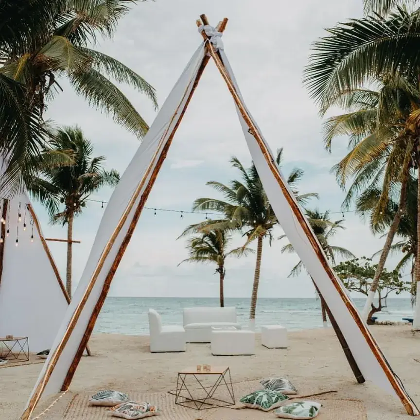 A-frame timber structure on the beach framed by palms and white lounge seating