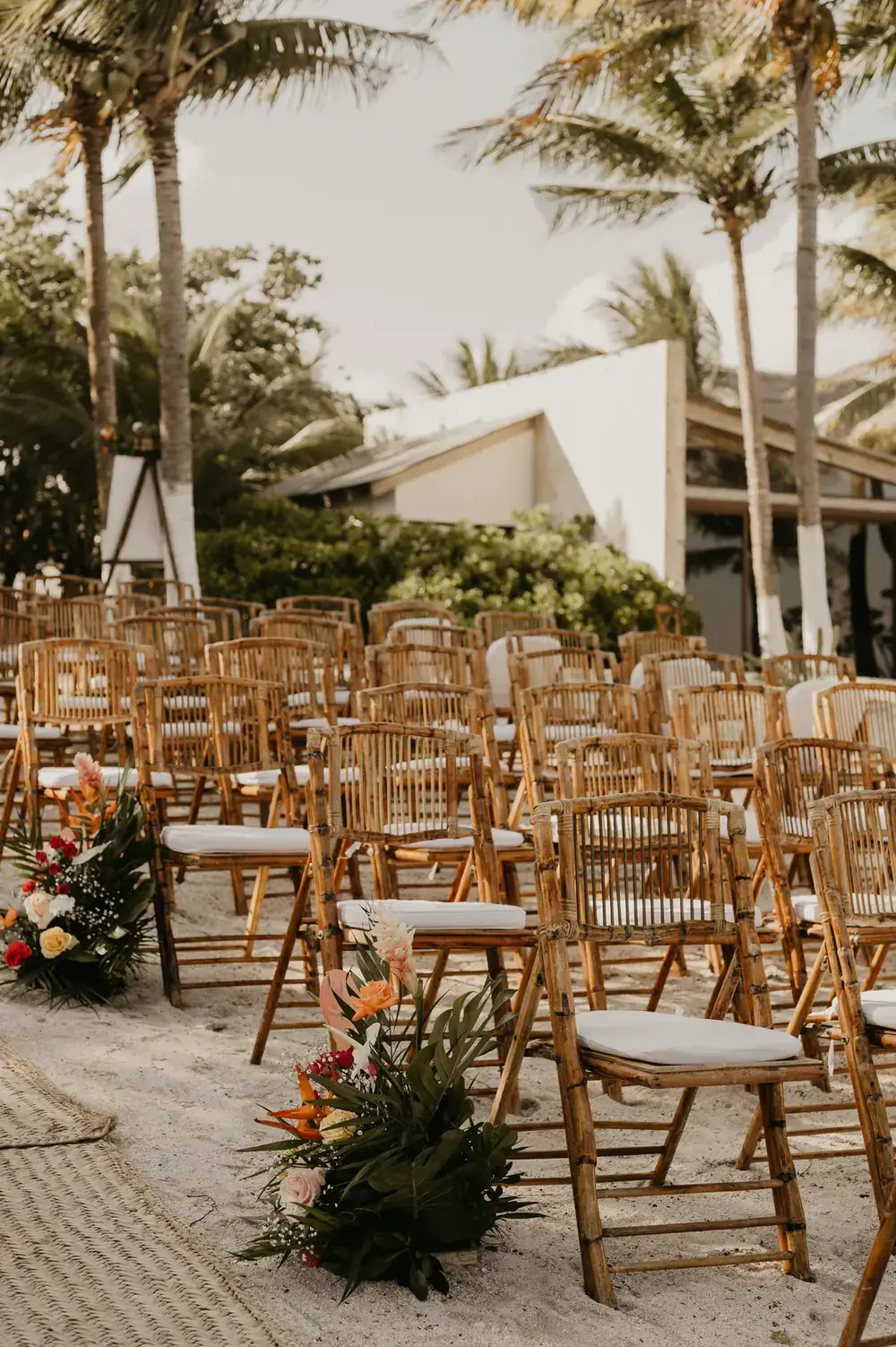 Rows of wooden ceremony chairs on the sand with florals lining the aisle