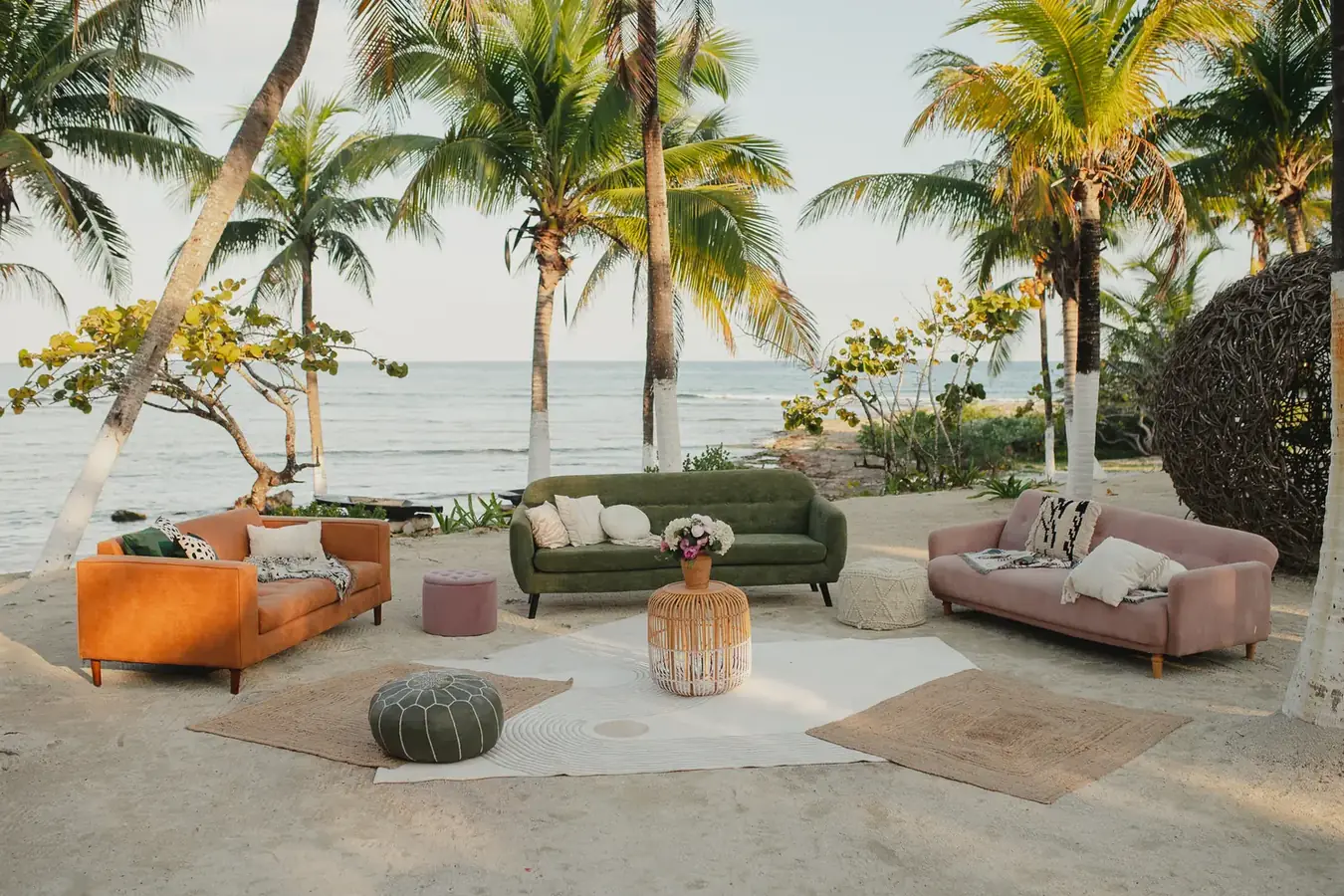 Beach lounge set with coloured sofas and woven poufs facing the ocean