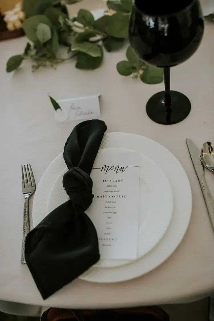 Place setting with a knotted black napkin, eucalyptus and a printed menu