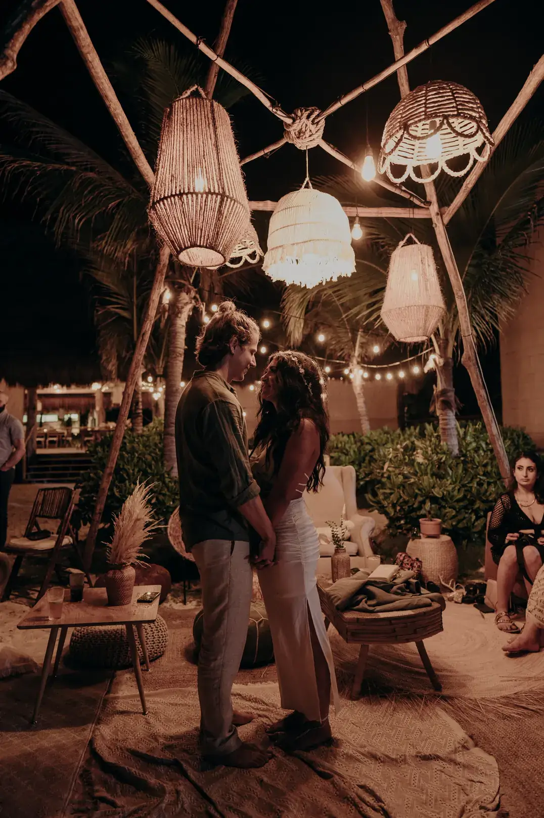 Couple standing together at night beneath woven lanterns and string lights