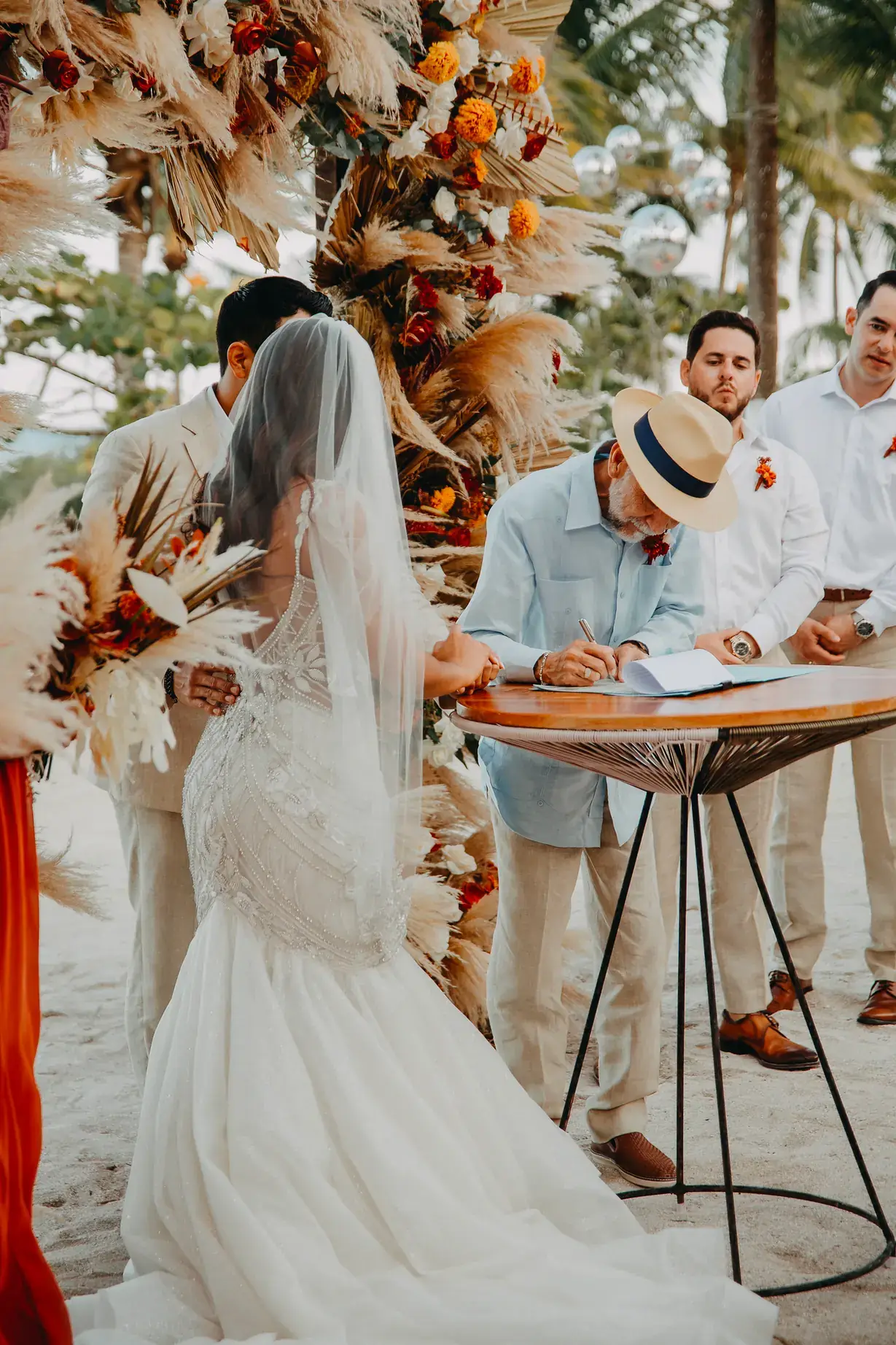 Bride and groom signing beside an installation of orange florals and pampas