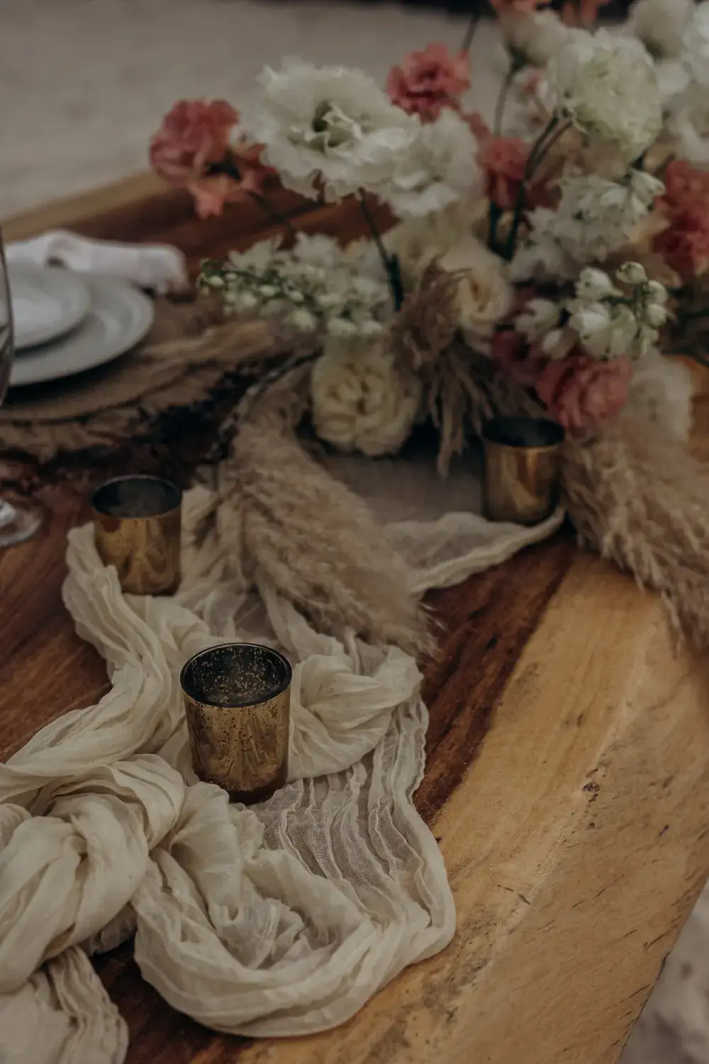 Close detail of a dried floral runner with cheesecloth and amber glass on a wooden table