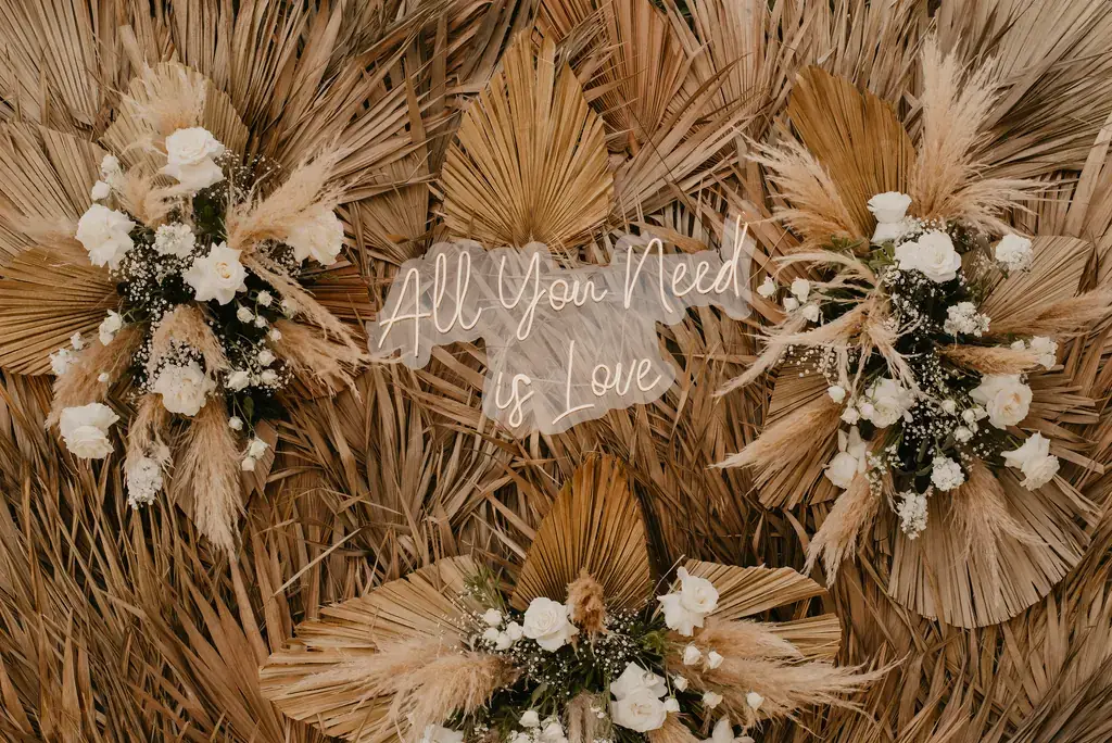 Backdrop of dried palm fans with a neon script sign