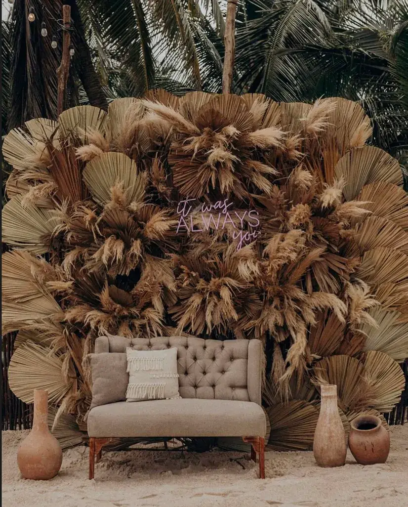 Dried palm fan installation behind a tufted sofa on the sand