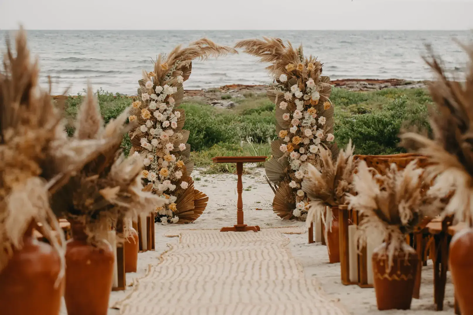 Beach ceremony arch dressed in pampas and dried florals at the end of a sand aisle, Riviera Maya
