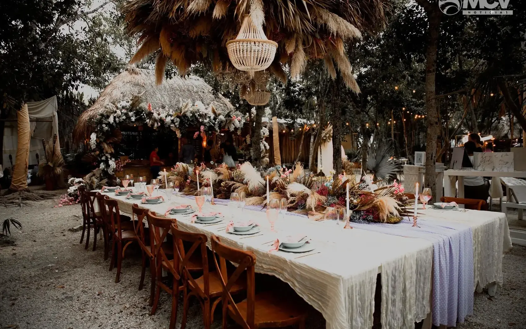 Banquet table under a jungle canopy at night, lit low, dressed with dried florals