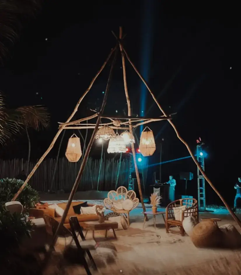 Timber teepee lit blue at night with lanterns and lounge seating