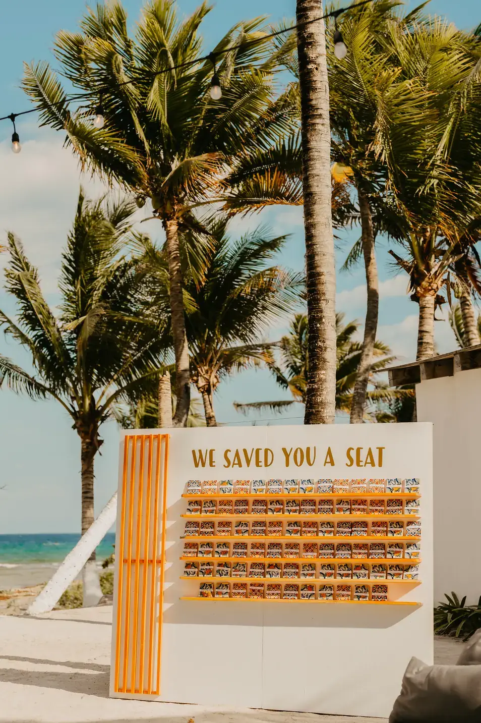 Orange seating chart wall on the beach framed by palms