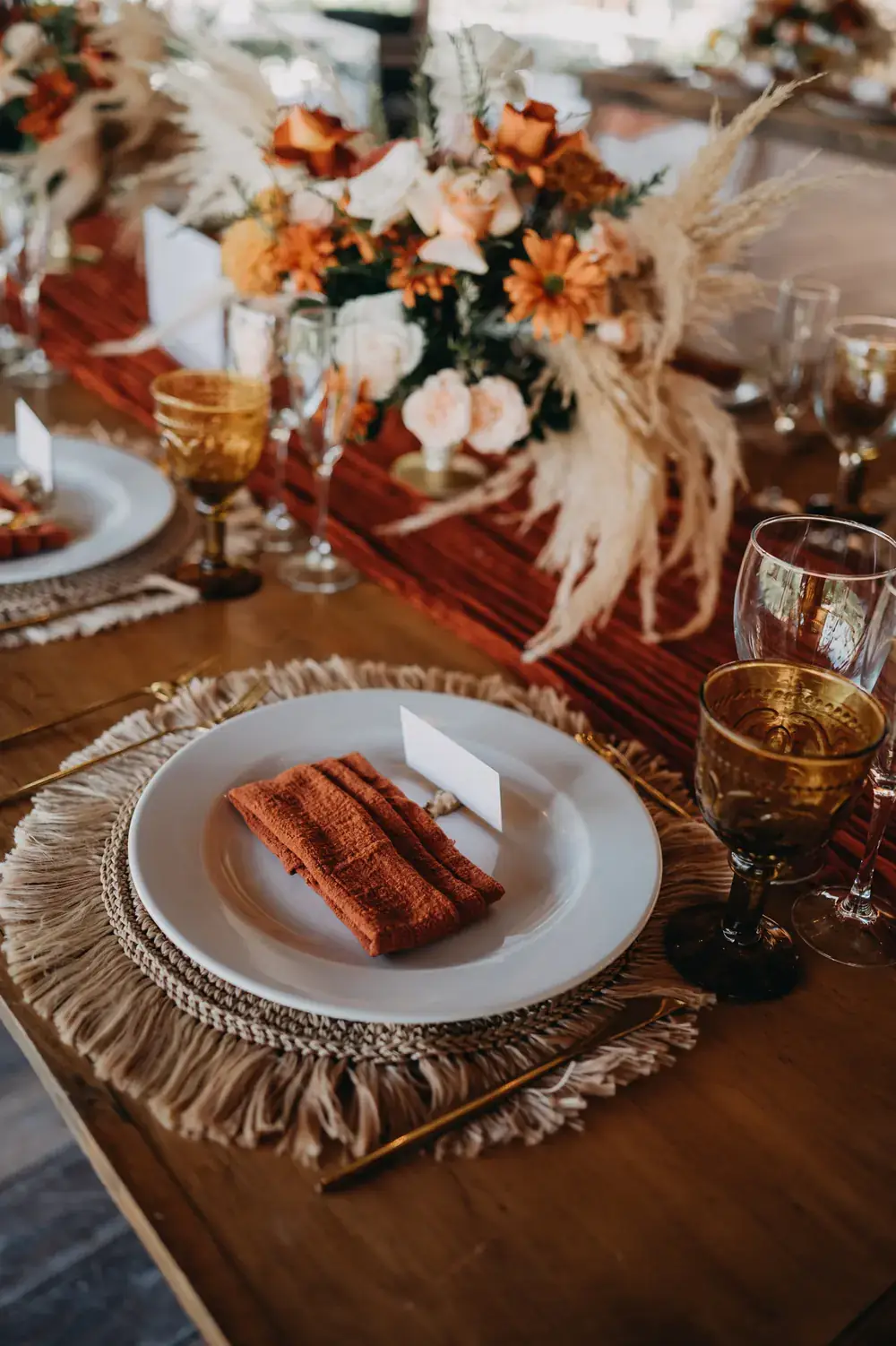 Tablescape with orange florals, pampas and fringed placemats