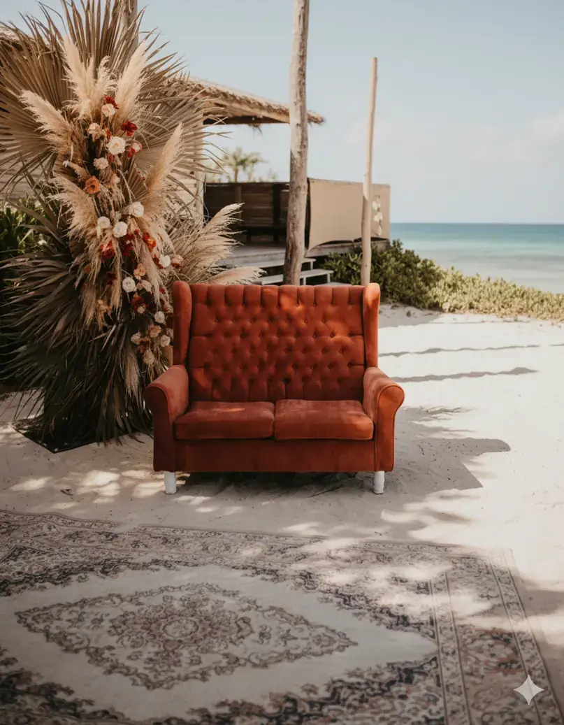 Burnt orange velvet sofa on the sand beside a floral installation