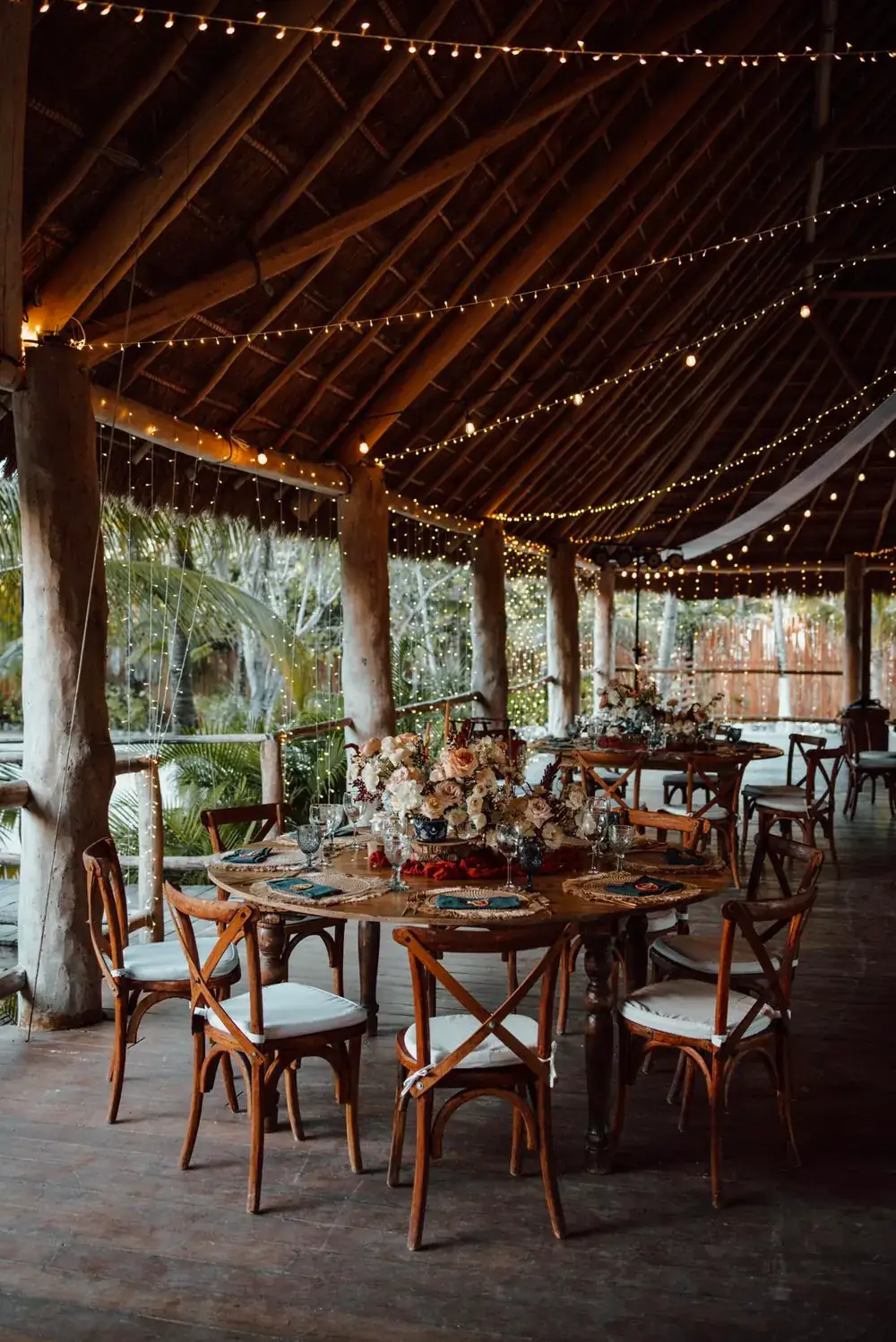 Round tables under a palapa roof strung with warm festoon lighting