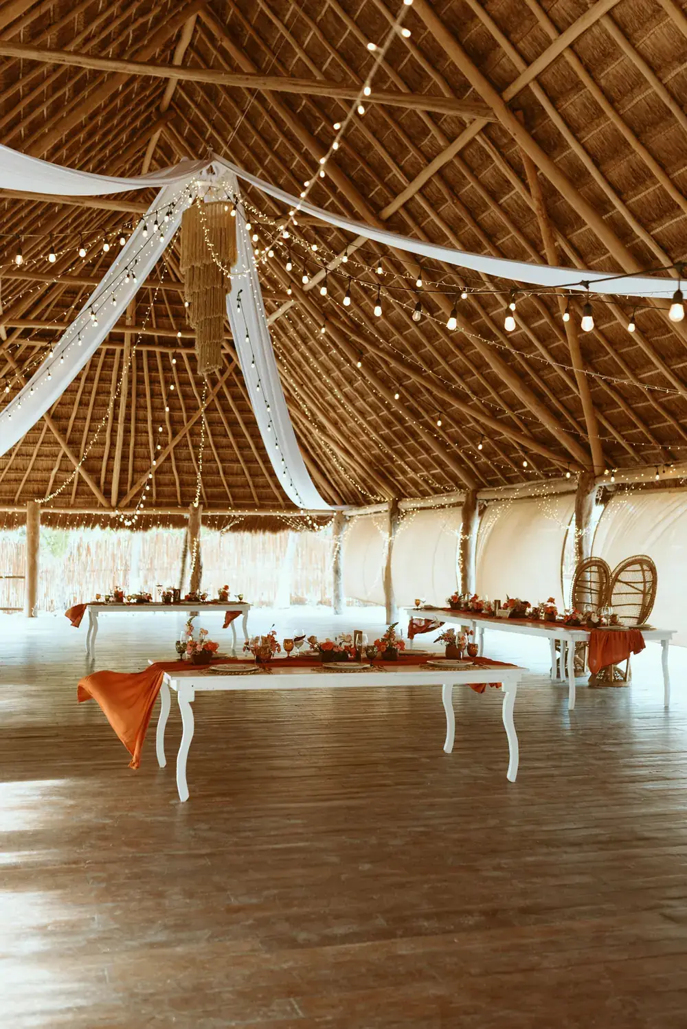 Palapa interior with white drapery falling from the roof over a long table