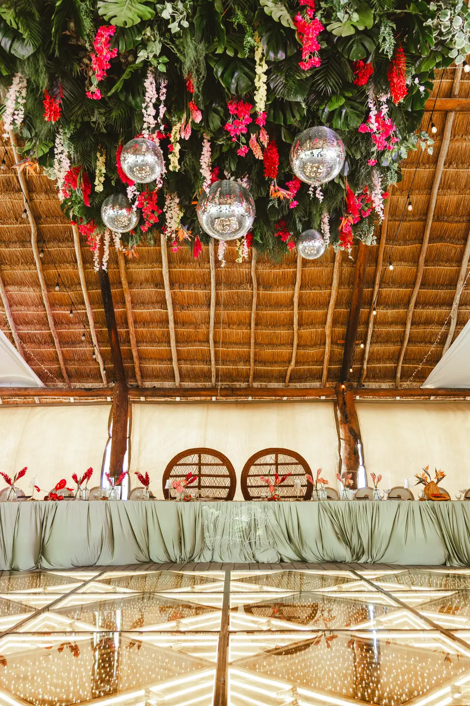 Hanging tropical floral installation with disco balls above a wedding sweetheart table