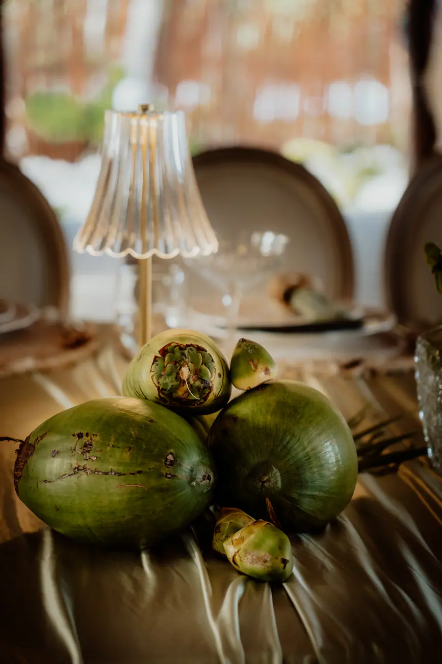 Green coconuts and artichokes composed as a wedding centerpiece on gold draping