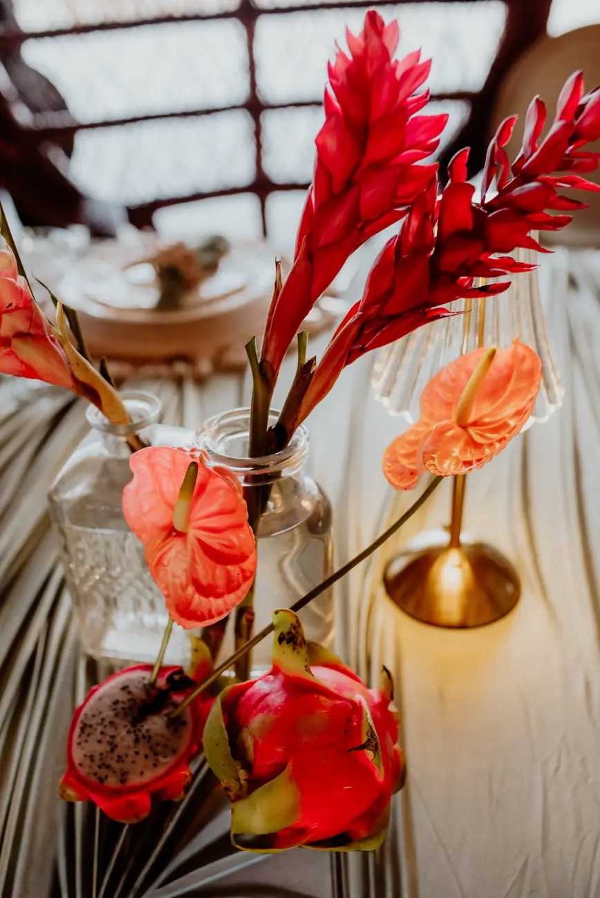 Red ginger, anthuriums and dragon fruit in clear bud vases on a wedding table