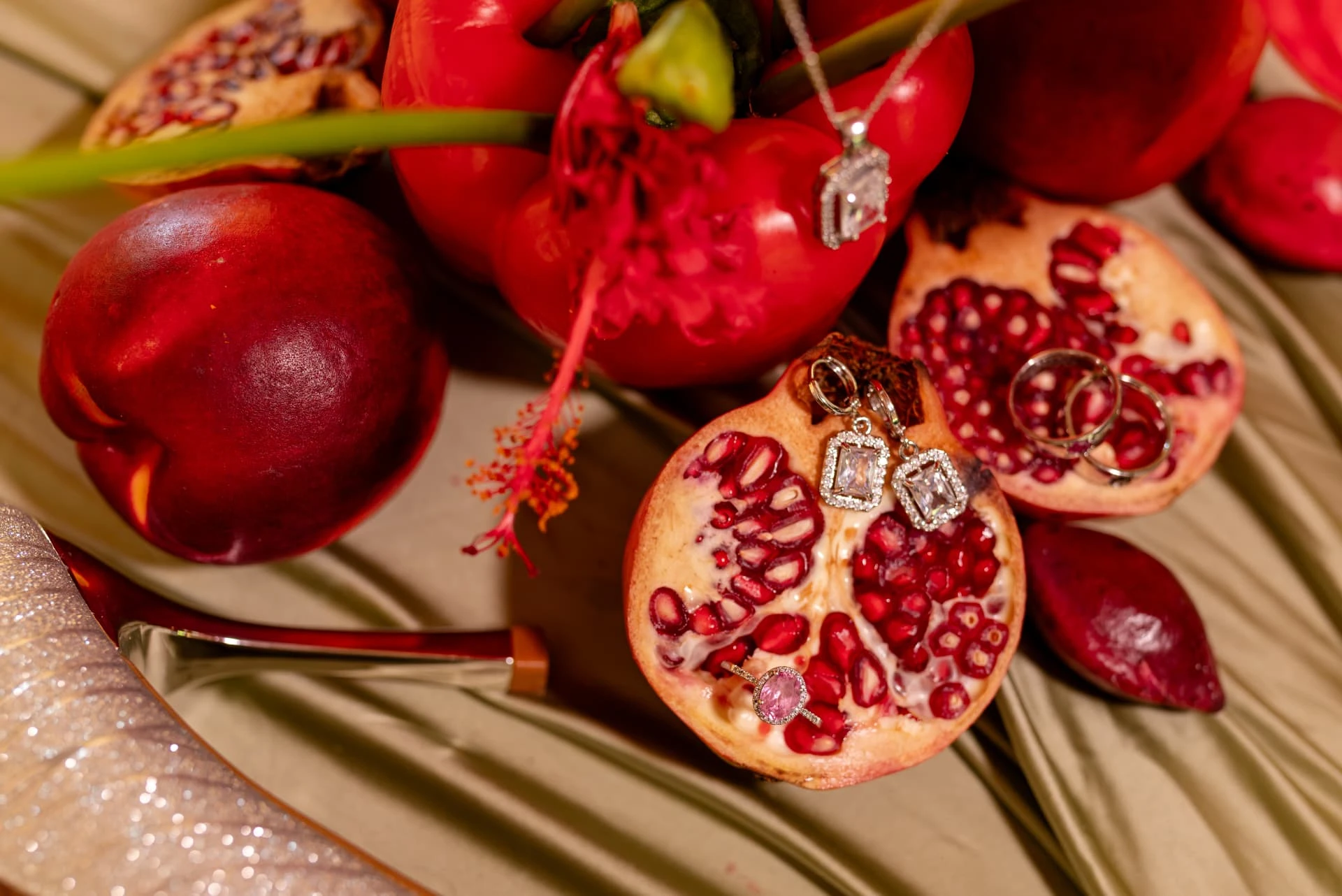 Diamond earrings, wedding bands and a pink sapphire ring resting on halved pomegranates with red fruit and hibiscus