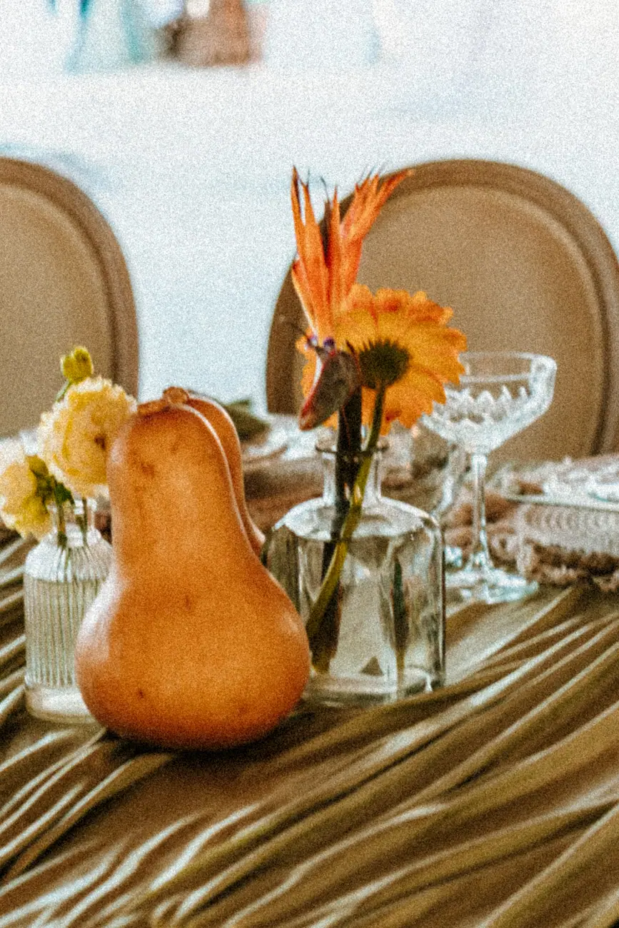 Pear and single stems in glass bud vases on olive overcloth draping at a tropical wedding table