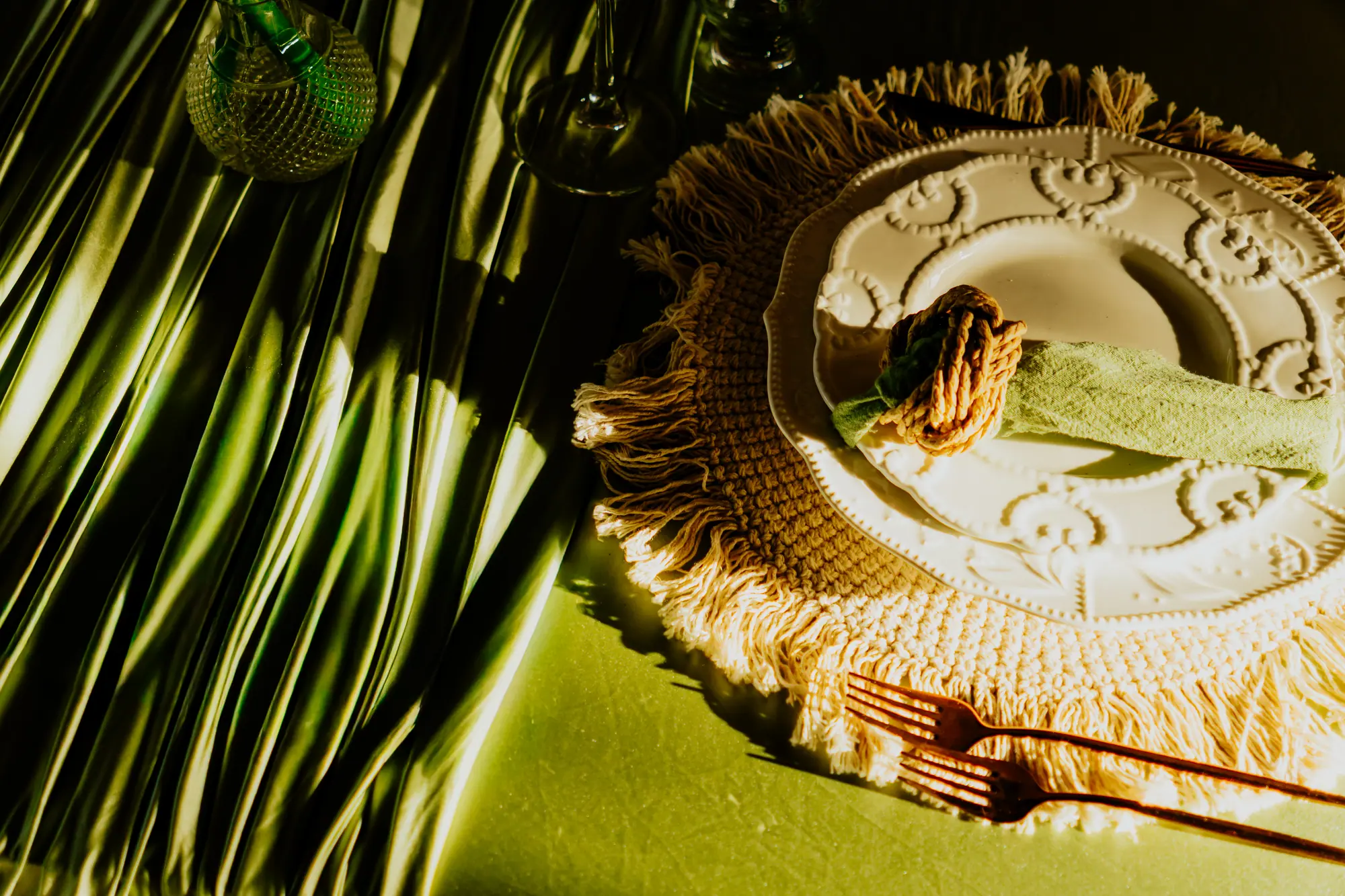 Wedding place setting with a crochet placemat, embossed plate, green napkin and copper flatware beside palm shadows