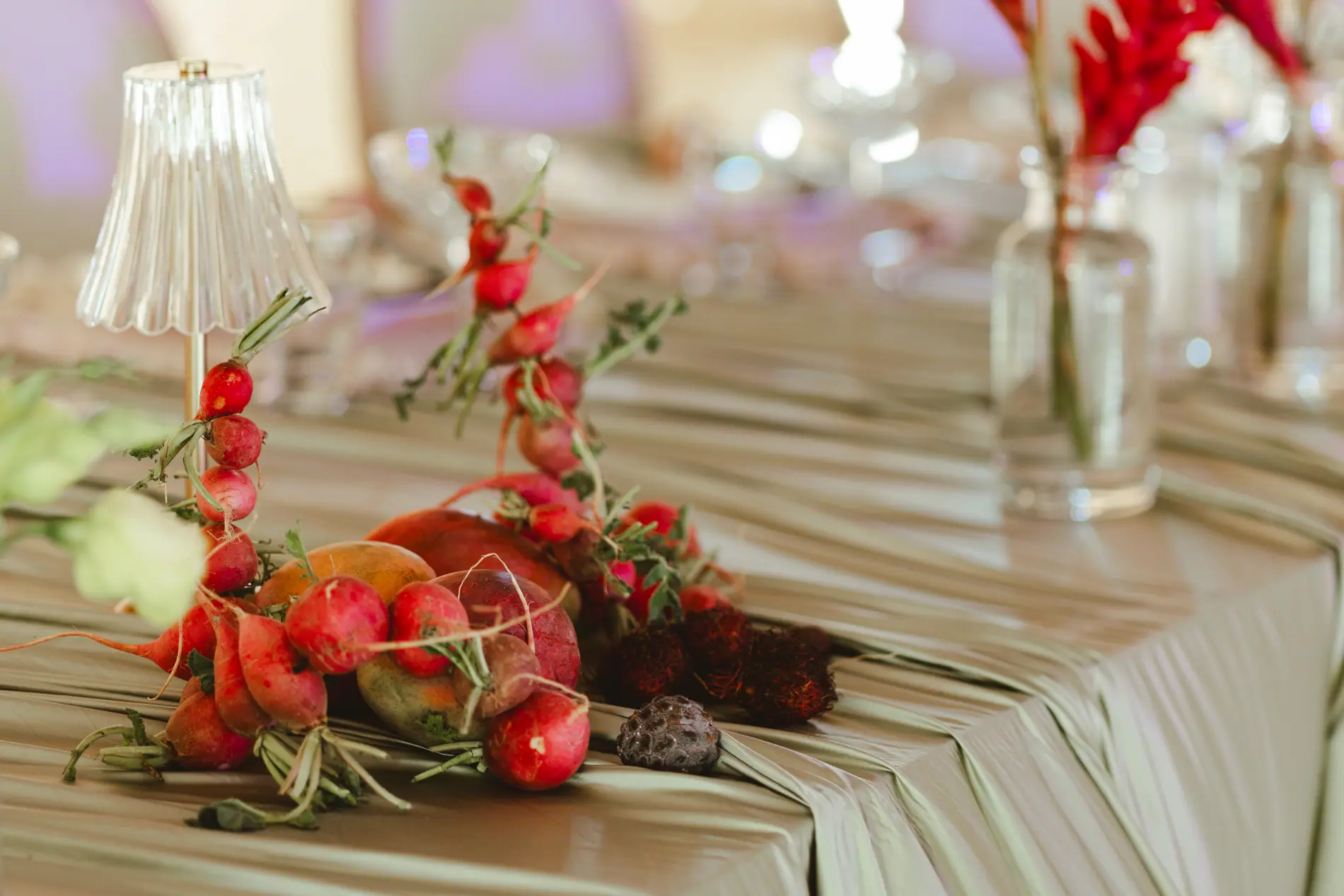 Radishes and tropical fruit running along olive overcloth draping down a long wedding table