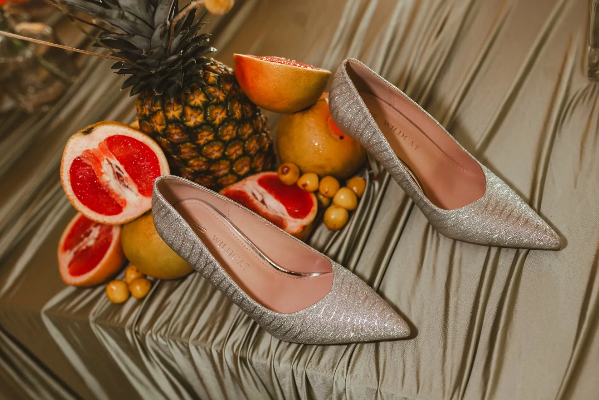 Silver glitter high-heeled pumps arranged with a whole pineapple and halved grapefruits on gathered satin