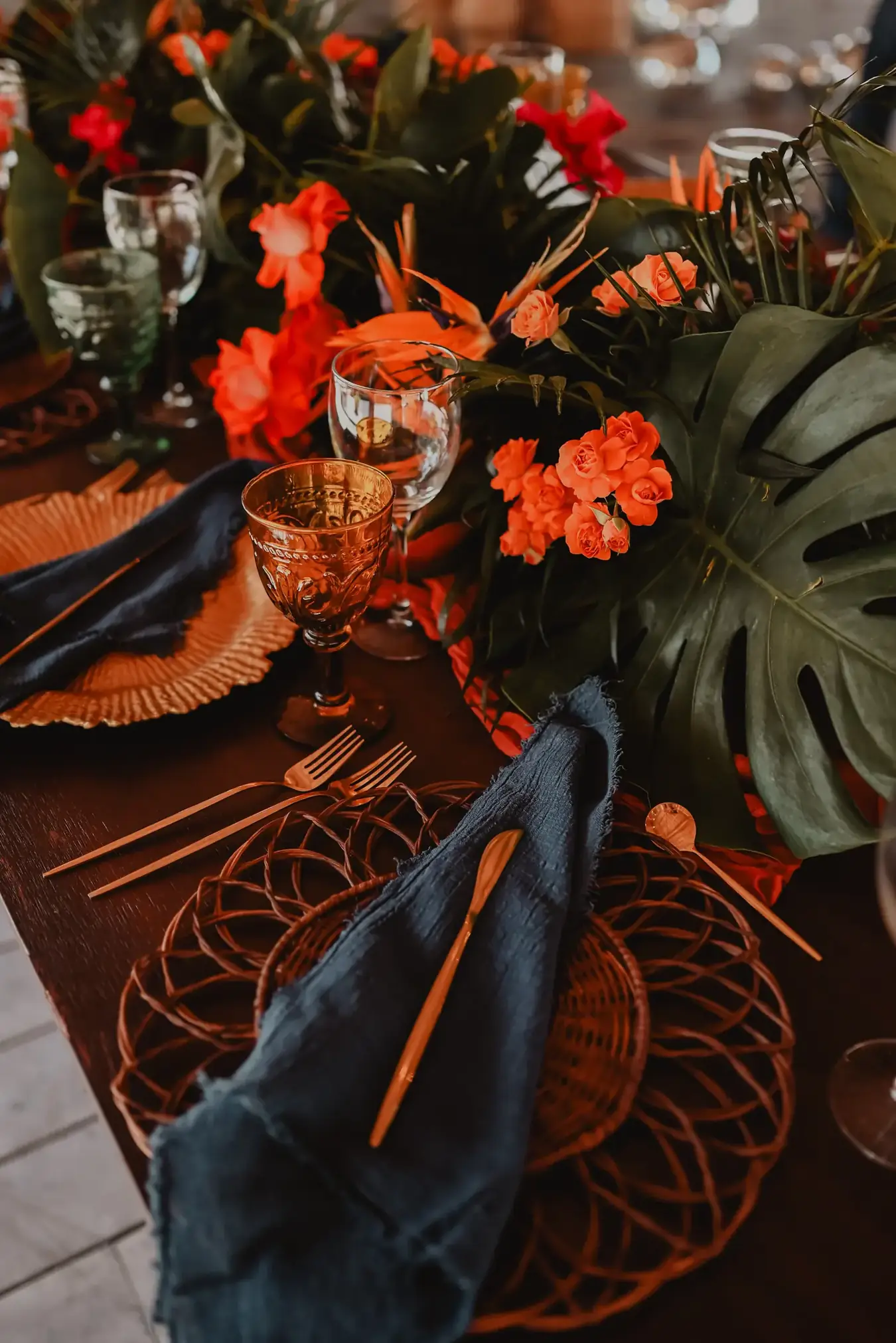 Saturated red and orange tropical tablescape with monstera leaves and coral glassware