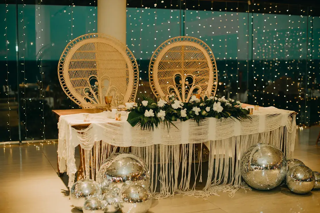 Sweetheart table backed in teal drapery with peacock chairs and hanging mirror balls