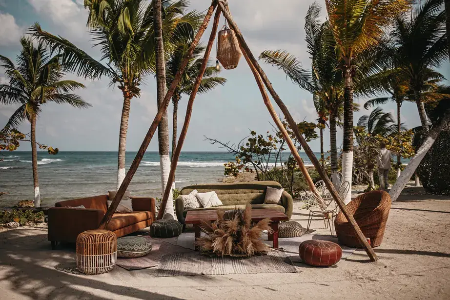 Beach lounge beneath a timber teepee with woven furniture and ocean behind