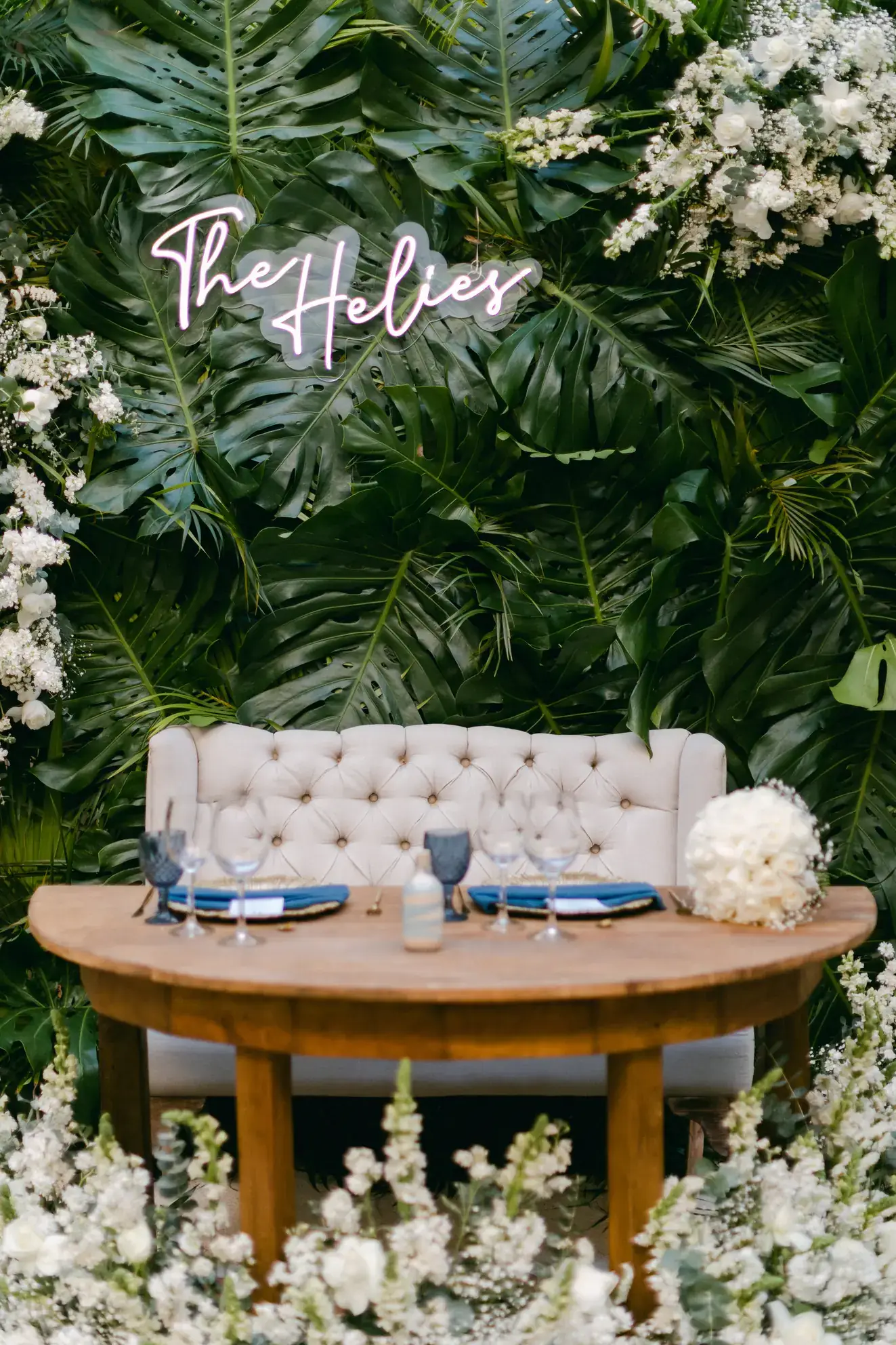 Wall of white florals and greenery behind a tufted sofa and low round table